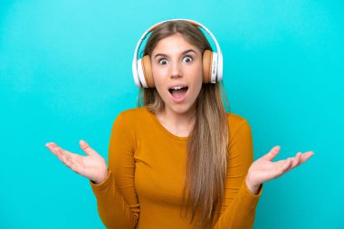 Mavi arka planda izole edilmiş genç beyaz kadın şaşırdı ve müzik dinliyor.