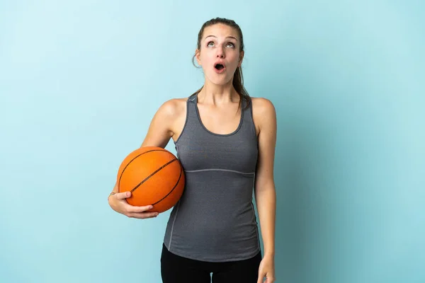 年轻女子在蓝底孤零零地打篮球 抬起头来 满脸诧异 — 图库照片