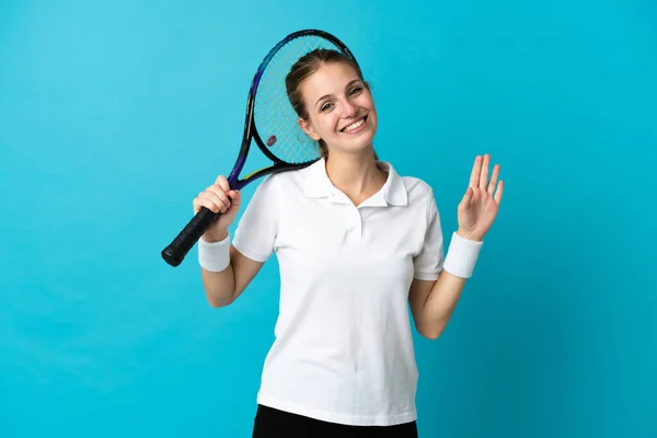 若いです女性テニスプレーヤー孤立しました上の青背景敬礼とともに幸せな表情 — ストック写真