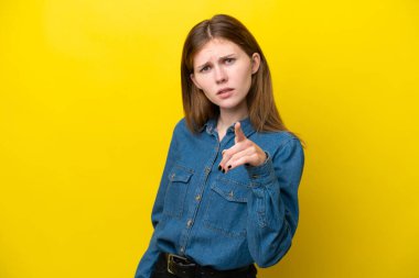 Sarı arka planda izole edilmiş genç bir İngiliz kadın hayal kırıklığına uğramış ve ön tarafı işaret ediyor.