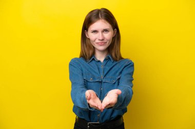 Sarı arka planda izole edilmiş genç bir İngiliz kadın bir ilan vermek için avucunun içinde hayali bir alan tutuyor.