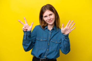 Sarı arka planda izole edilmiş genç İngiliz kadın parmaklarıyla sekiz sayıyor.