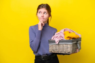 Sarı arka planda izole edilmiş çamaşır sepetini tutan genç İngiliz kadının şüpheleri ve düşünceleri var.