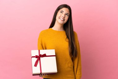 Genç Brezilyalı bir kız pembe arka plan üzerinde bir hediye tutuyor ve yukarı bakarken bir fikir düşünüyor