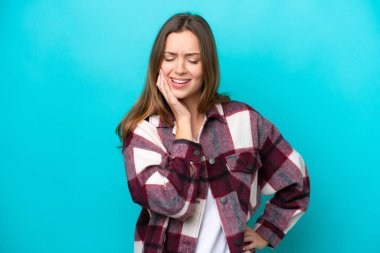 Mavi arka planda diş ağrısı çeken genç beyaz bir kadın.