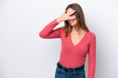 Beyaz arka planda soyutlanmış beyaz tenli genç bir kadın elleriyle gözlerini kapatıyor ve gülümsüyor.