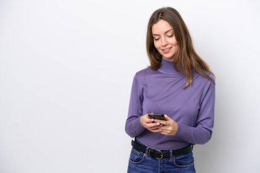 Beyaz arka planda izole edilmiş genç beyaz kadın cep telefonuyla mesaj gönderiyor.