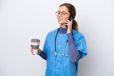 Beyaz arka planda izole edilmiş beyaz bir hemşire elinde kahve ve cep telefonu olan genç bir kadın.