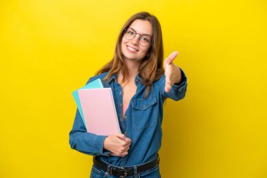 Sarı arka planda izole edilmiş genç beyaz kadın iyi bir anlaşma için el sıkışıyor.