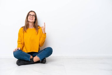 Beyaz arka planda izole bir şekilde yerde oturan beyaz bir kadın yukarı bakıyor ve şaşırıyor.