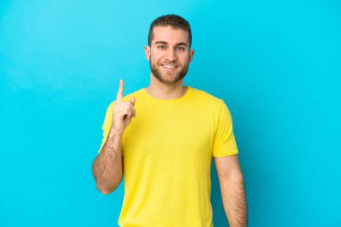 Mavi arka planda izole edilmiş yakışıklı beyaz adam harika bir fikre işaret ediyor.