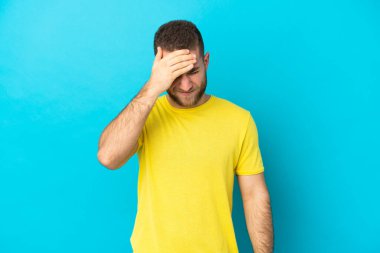 Mavi arka planda yalnız ve başı ağrıyan yakışıklı beyaz bir adam.