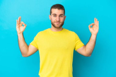 Zen pozunda mavi arka planda izole edilmiş yakışıklı beyaz bir adam.