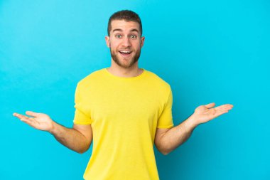 Yüzünde şok ifadesi olan, mavi arka planda izole edilmiş, yakışıklı beyaz bir adam.