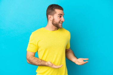 Mavi arka planda mahsur kalmış yakışıklı, beyaz bir adam.