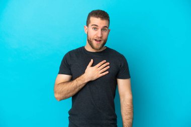 Mavi arka planda izole edilmiş yakışıklı beyaz adam sağa bakarken şaşırdı ve şok oldu.