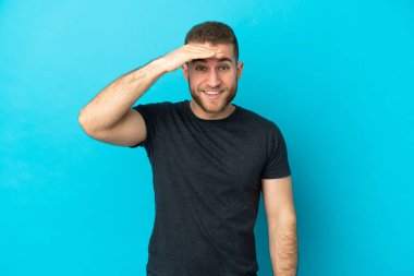 Mavi arka planda izole edilmiş yakışıklı beyaz bir adam. Bir şeye bakmak için uzaklara bakıyor.