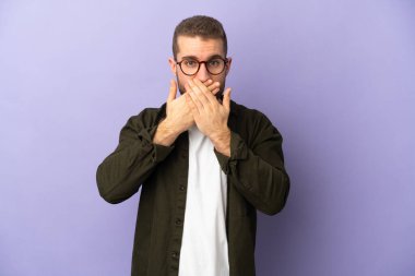 Mor arka planda izole edilmiş yakışıklı beyaz adam elleriyle ağzını kapatıyor.
