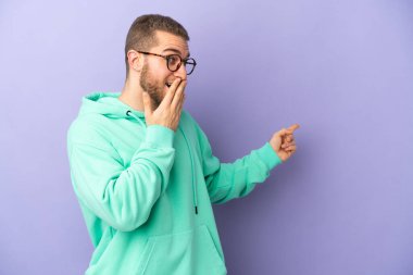 Mor arka planda izole edilmiş yakışıklı beyaz bir adam sürpriz bir ifadeyle işaret ederken...