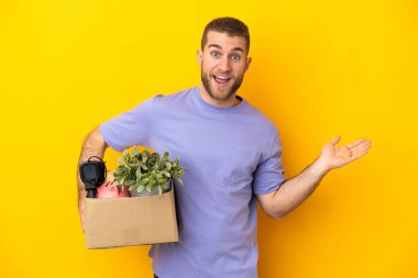 Genç Kafkasyalı, sarı arka planda izole edilmiş ve şok olmuş yüz ifadesiyle dolu bir kutu alırken hamle yapıyor.