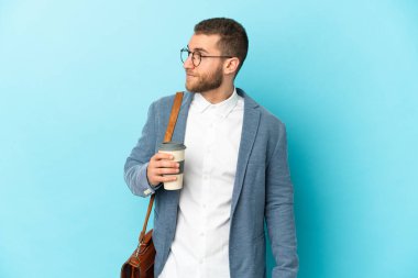 Kafkasyalı genç işadamı mavi arka planda izole edilmiş, yan tarafa bakıyor.