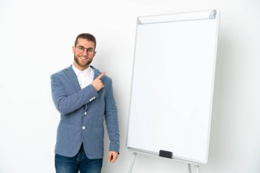 Beyaz arka planda izole edilmiş beyaz panoda sunum yapan genç bir iş kadını bir ürünü sunmak için kenarı işaret ediyor.