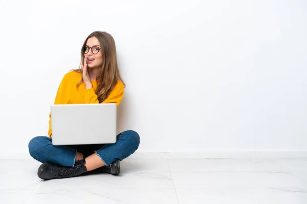 年轻的高加索女人 带着笔记本电脑坐在地板上 与白色背景隔离 低声说着什么 — 图库照片