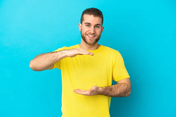 Homem Caucasiano Bonito Jovem Isolado Fundo Azul Segurando Copyspace Imaginário — Fotografia de Stock