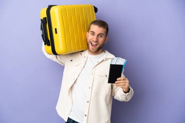 Mor arka planda izole edilmiş yakışıklı beyaz bir adam tatilde bavul ve pasaportla.