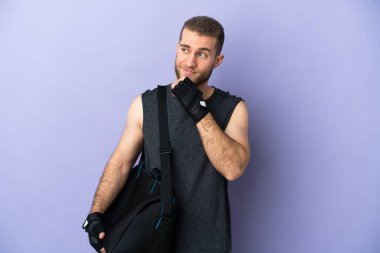 Spor çantalı genç adam beyaz arka planda izole edilmiş, yana bakıyor ve gülümsüyor.