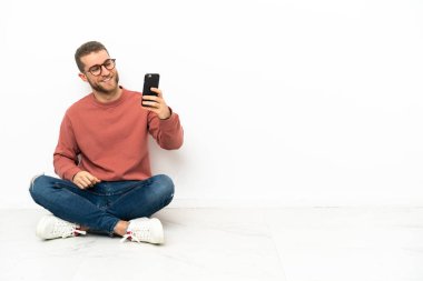 Genç yakışıklı bir adam yerde oturmuş selfie çekiyor.