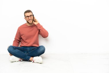 Yerde oturan yakışıklı genç adam cep telefonuyla sohbet ediyor.