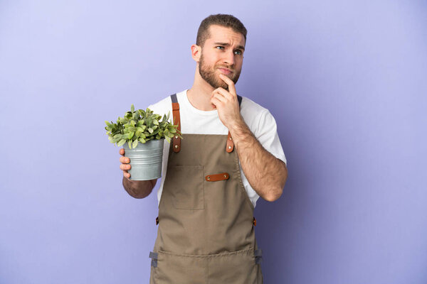 Gardener caucasian man holding a plant isolated on yellow background having doubts while looking up