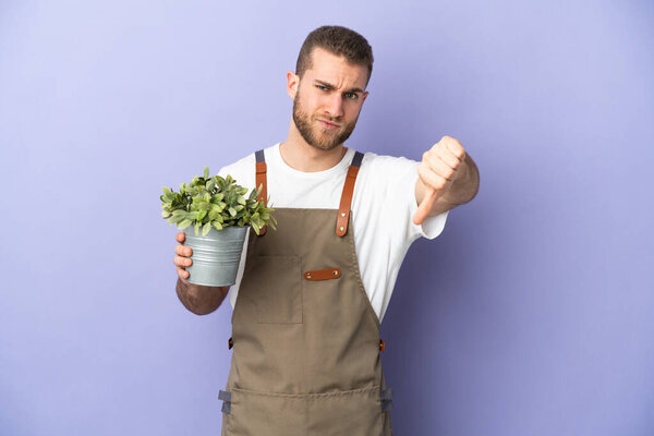 Gardener caucasian man holding a plant isolated on yellow background showing thumb down with negative expression