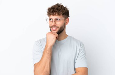 Beyaz arka planda gözlüklü ve düşünen beyaz tenli genç bir adam.