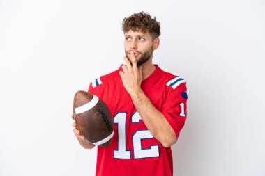 Beyaz arka planda ragbi oynayan genç beyaz bir adam yukarı bakarken şüphe duyuyor.