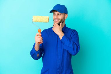 Kafkasyalı ressam mavi arka planda izole edilmiş, yana bakıyor ve gülümsüyor.