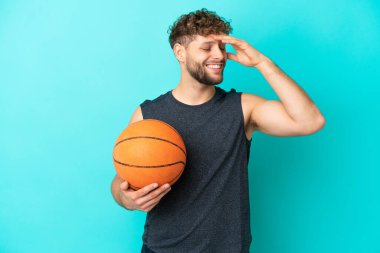 Basketbol oynayan yakışıklı genç adam mavi arka planda izole edilmiş, çok gülümsüyor.