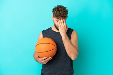 Basketbol oynayan yakışıklı genç adam mavi arka planda izole edilmiş, yorgun ve hasta bir ifadeyle.