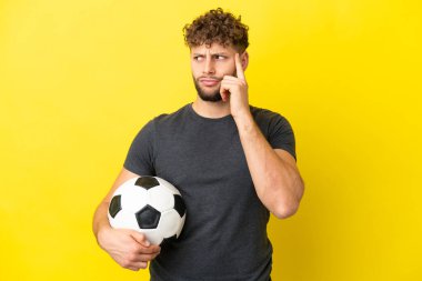 Yakışıklı genç futbolcu sarı arka planda izole edilmiş kuşkuları ve düşünceleri var.
