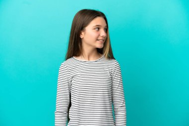 Küçük kız soyutlanmış mavi arka planda, yana bakıyor ve gülümsüyor.