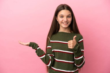 İzole edilmiş pembe arka plan üzerinde küçük bir kız. Avucunun içinde hayali bir şey tutuyor. Bir ilan vermek için.