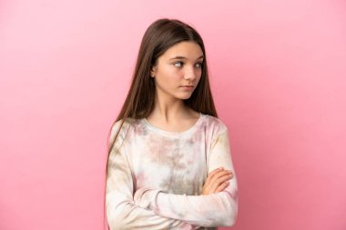 Küçük kız pembe arka planda kollarını kavuşturuyor.