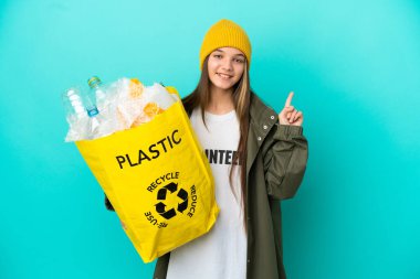 Küçük kız, izole edilmiş mavi arka planda geri dönüşüm yapmak için plastik şişelerle dolu bir çanta tutuyor. Harika bir fikir.