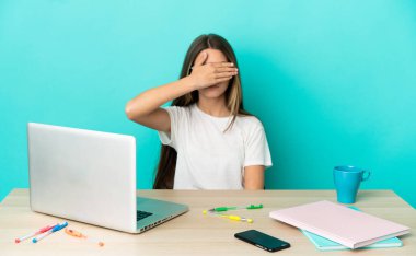 Masada dizüstü bilgisayarı olan küçük bir kız. İzole edilmiş mavi arka plan, gözleri elle kapatıyor. Bir şey görmek istemiyorum.