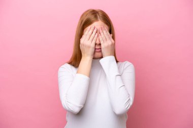 Genç kızıl saçlı kadın pembe arka planda izole edilmiş gözlerini elleriyle kapatıyor.