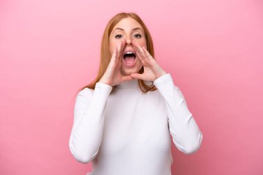 Genç kızıl saçlı kadın pembe arka planda izole edilmiş bağırıyor ve bir şeyler söylüyor.