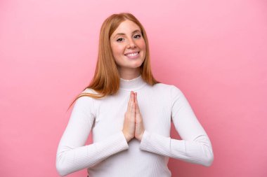 Pembe arka planda izole edilmiş genç kızıl saçlı kadın avuç içlerini bir arada tutuyor. İnsan bir şey ister.