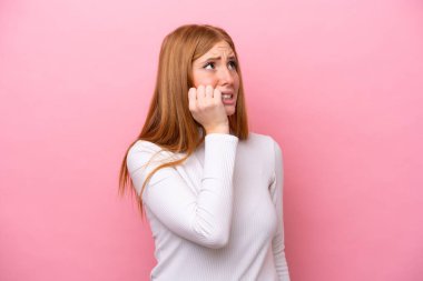 Pembe arka planda izole edilmiş genç kızıl saçlı kadın biraz gergin.