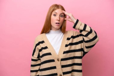 Pembe arka planda izole edilmiş genç kızıl saçlı kadın bir şey fark etti ve çözümü arıyor.